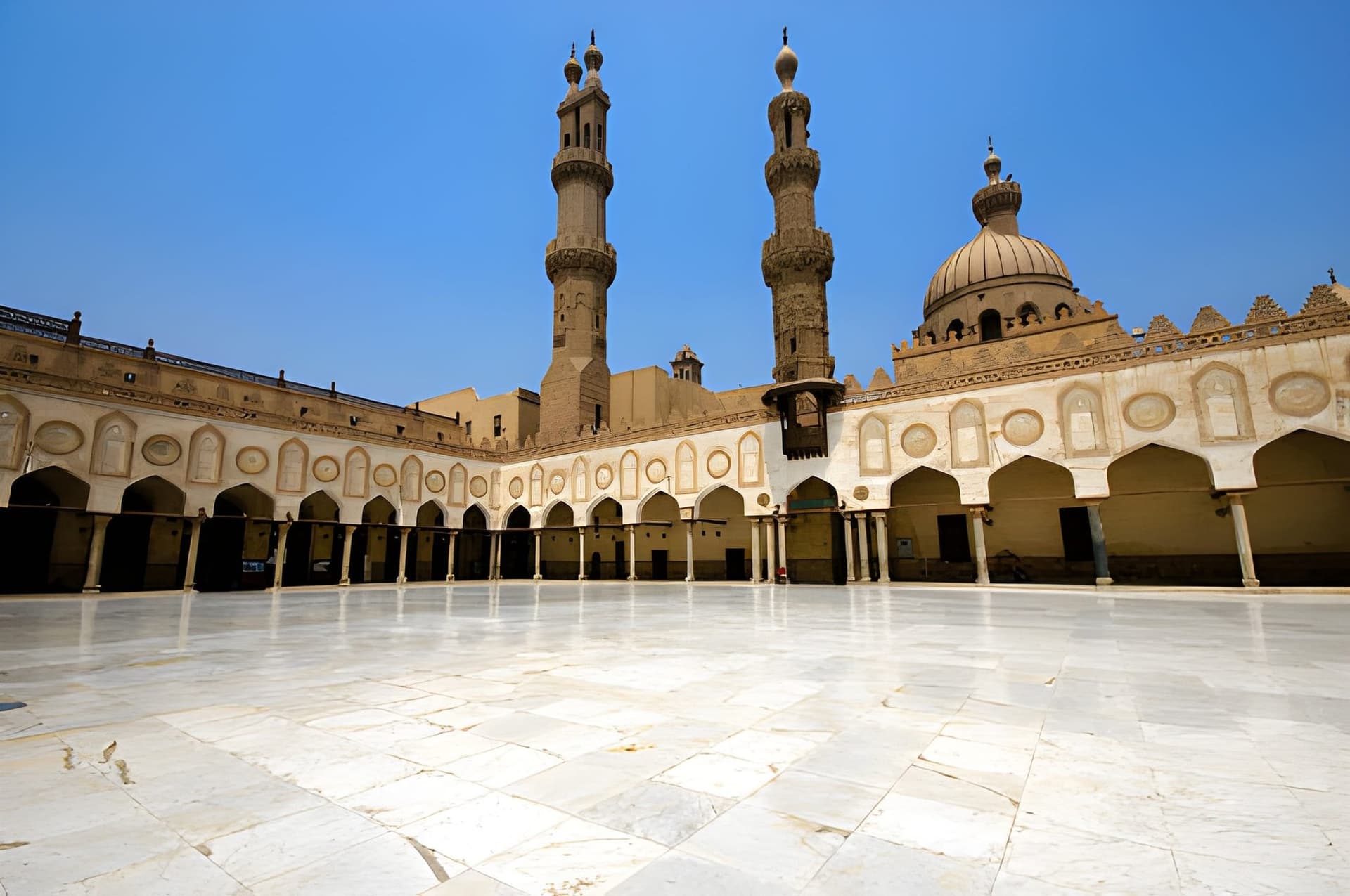 The white marble courtyard of Al-Azhar Mosque in Cairo, ringed by arcades, with its minarets against a clear sky