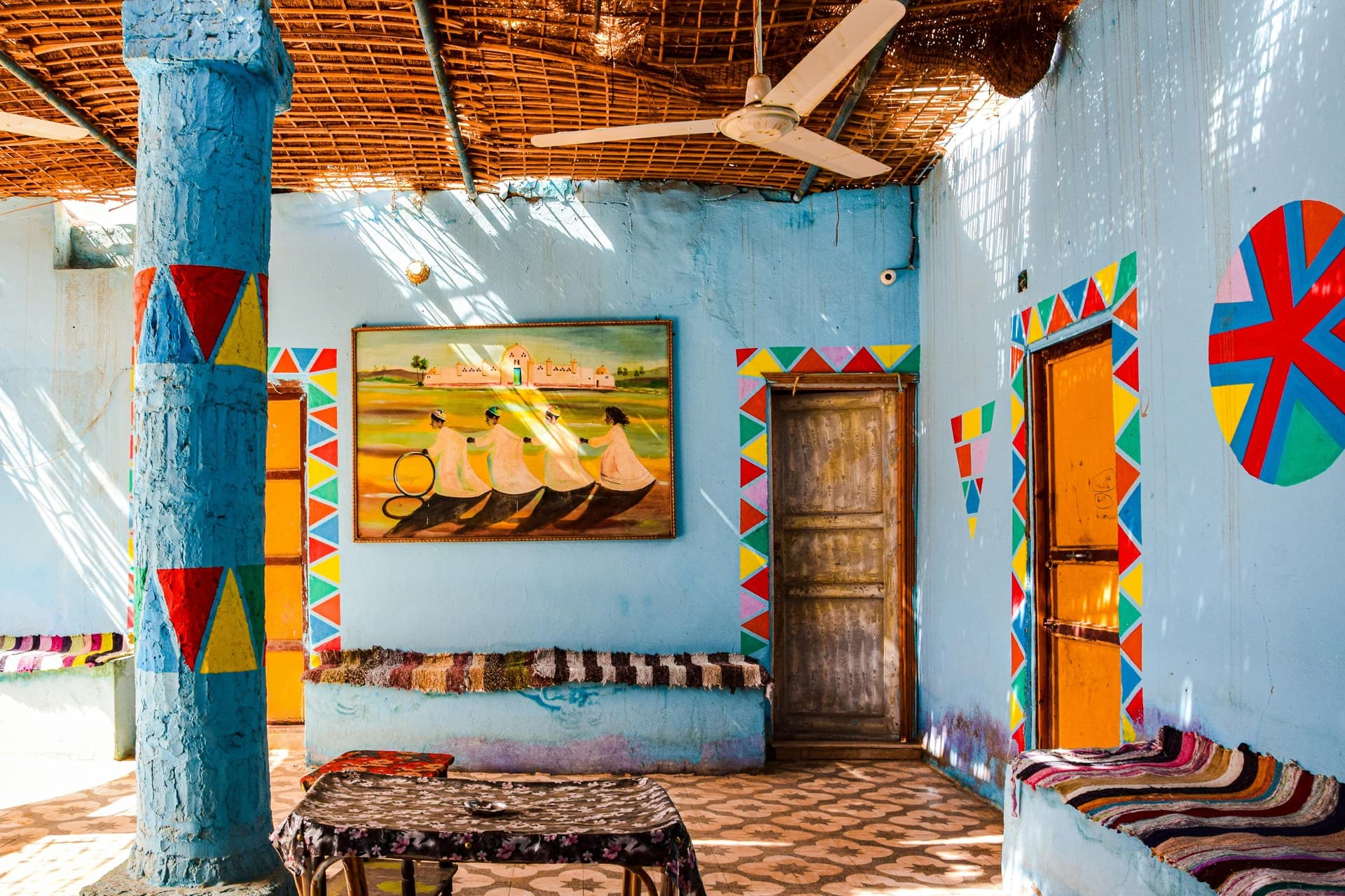 Brightly painted blue and ochre Nubian houses along a sandy lane above the Nile at Aswan