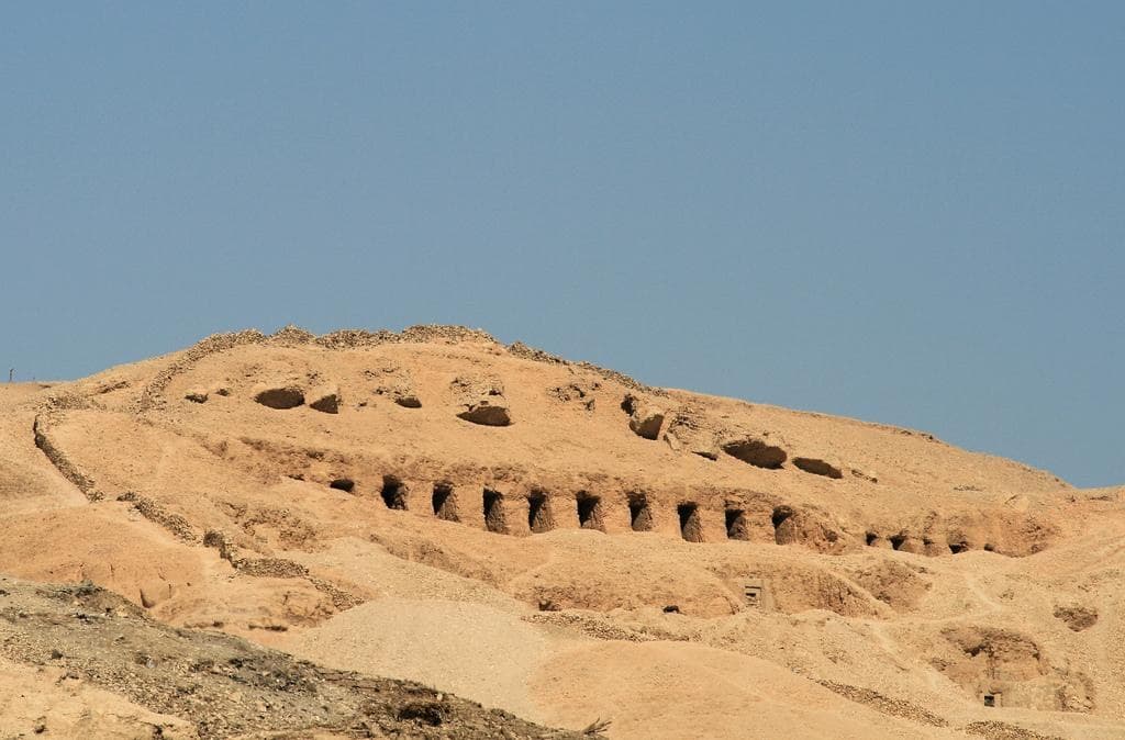 The bare hillside of the Valley of the Queens on the Luxor west bank with the row of rock-cut tomb entrances along it