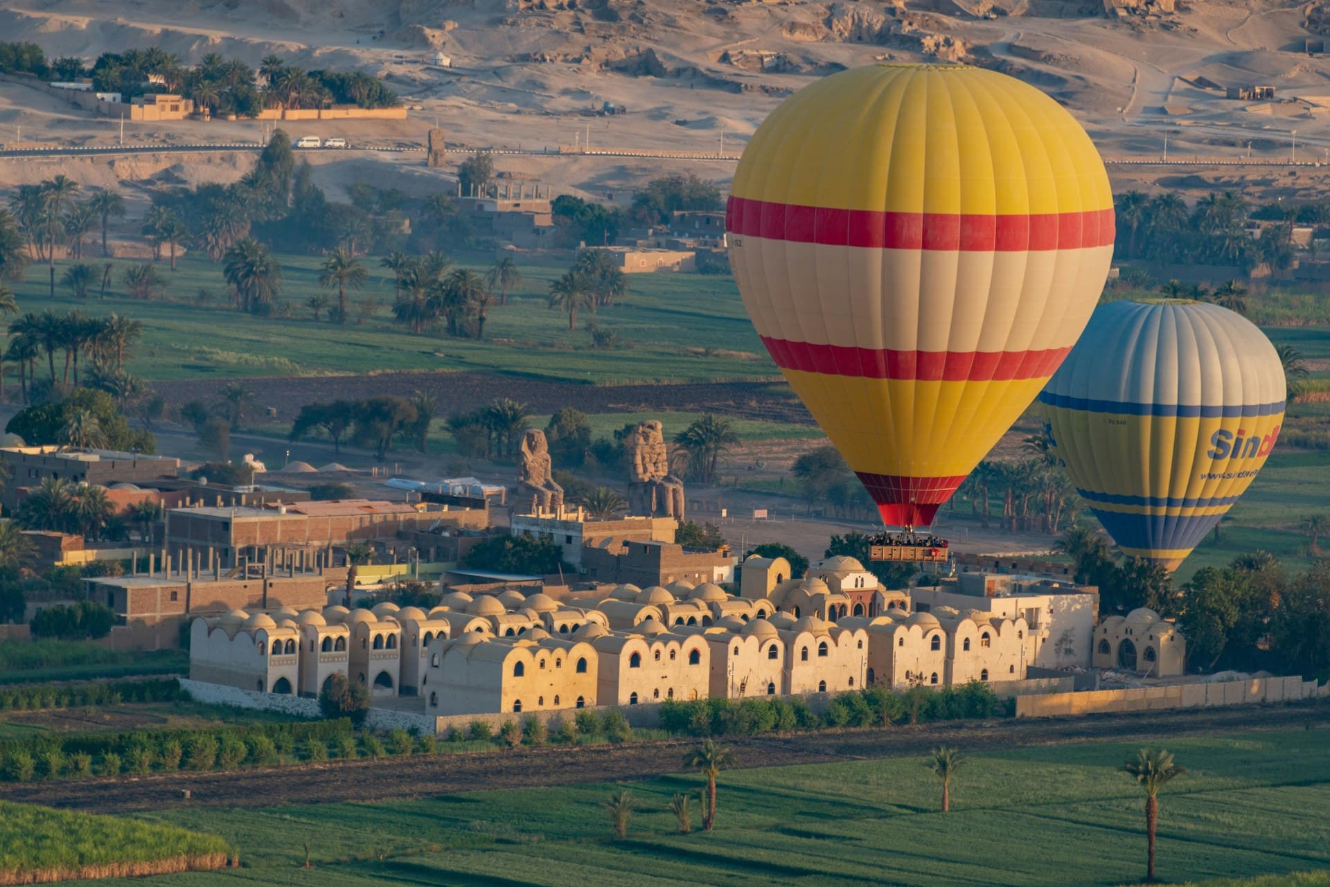 The Colossi of Memnon standing in farmland on the Luxor west bank